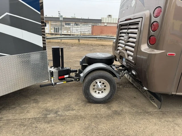A Trailer Toad with a spare tire on top, hitched behind a Class A motorhome. The weight distribution hitch's spring bar runs from the back of the Toad to the trailer.